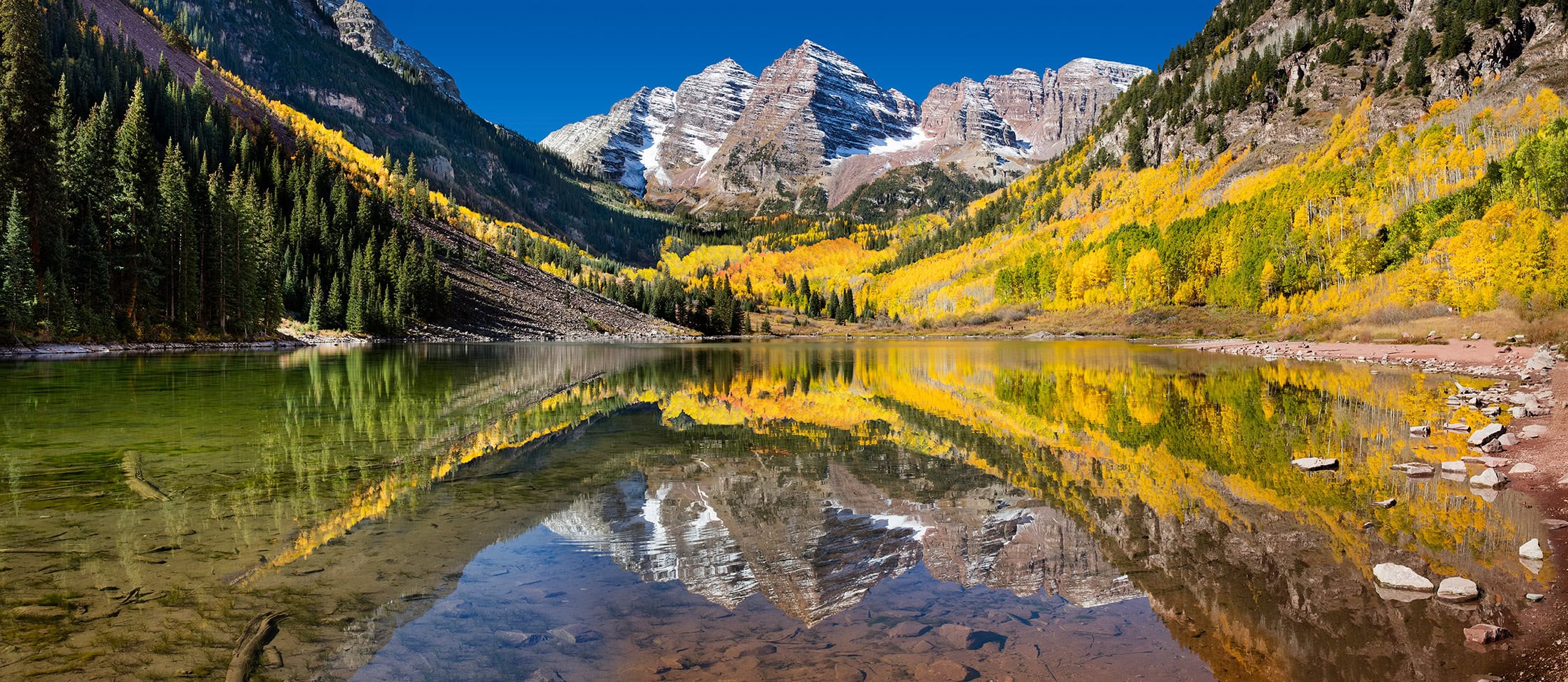 A mountain range mirrored in a clear alpine lake, aspen gold on both slopes