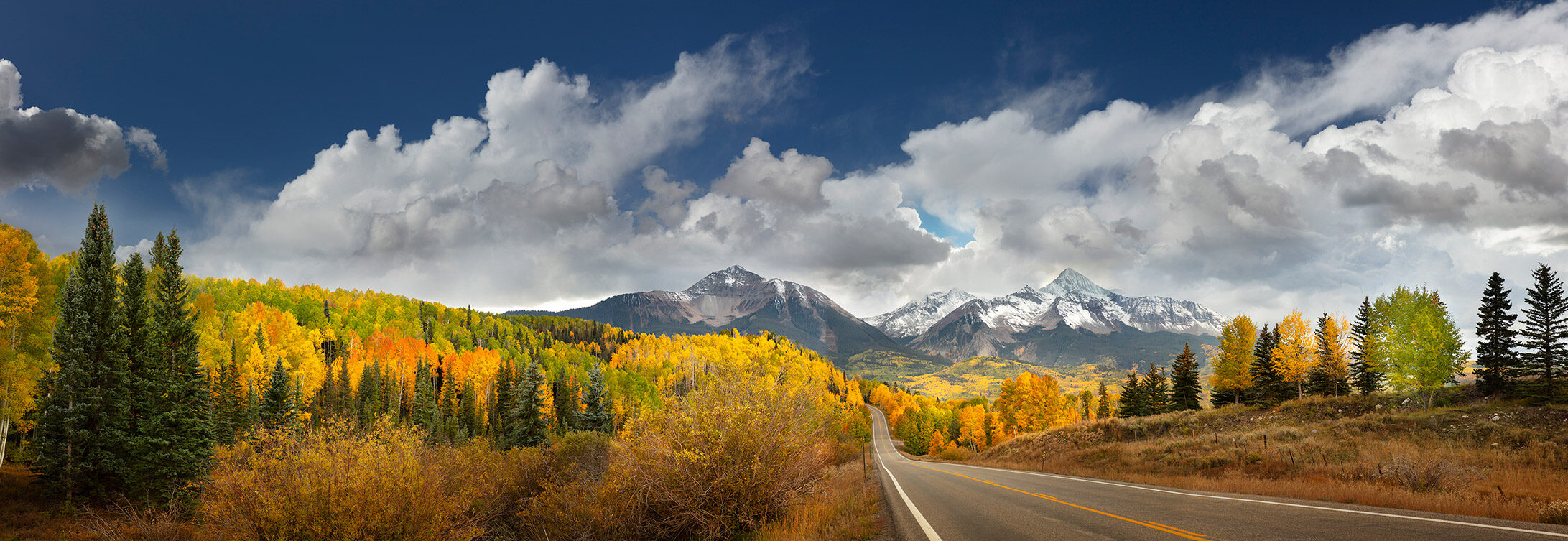 A highway curving through autumn colour toward snow-covered peaks